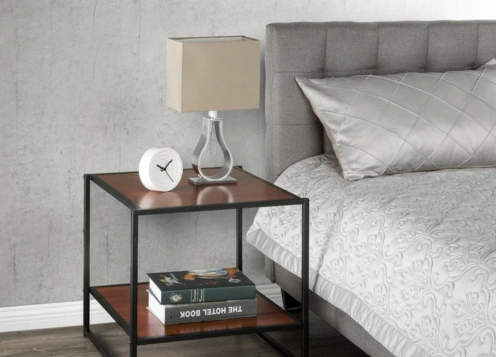 A  bedside table with a black metal frame upper shelves with a lamp, clock & lower shelves with books.