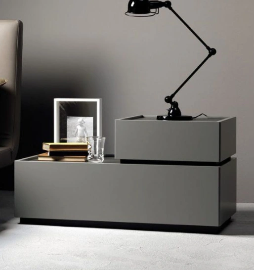 A gray-finished bedside table with two stacked drawers features a lamp, photo glass frame & books on top.