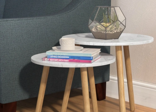 A round marble-top side table with books and a cup, adjacent to a geometric terrarium, beside a grey sofa.