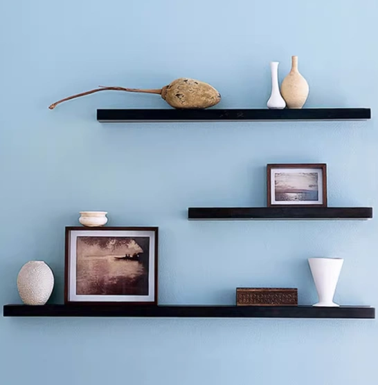 A blue wall with three neatly arranged shelves, showcasing a vase that adds elegance to the space.